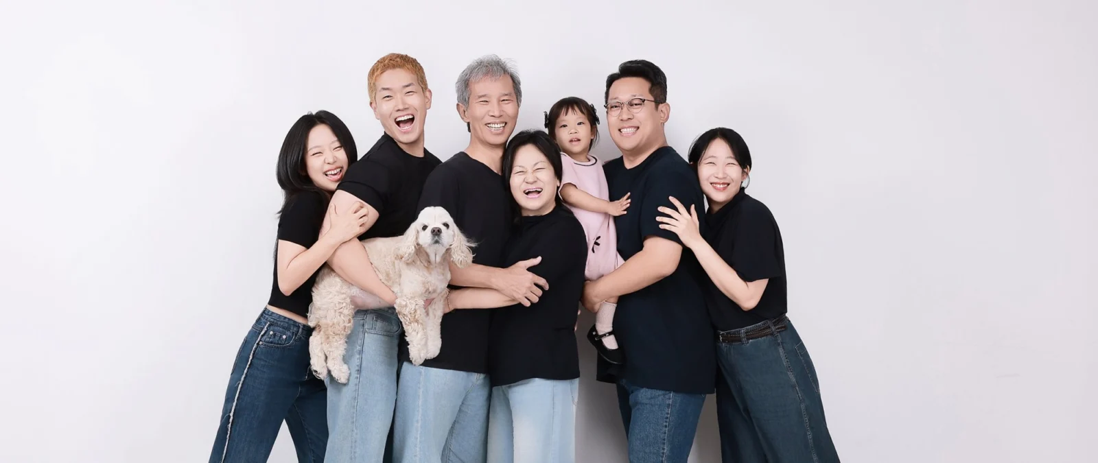 검은 티셔츠 가족 여덟 명이 흰 강아지를 안고 웃는 가로 개족사진