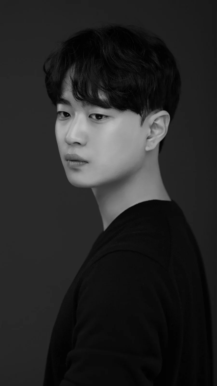 어두운 배경에서 짧은 머리로 정면을 보는 흑백 프로필 사진