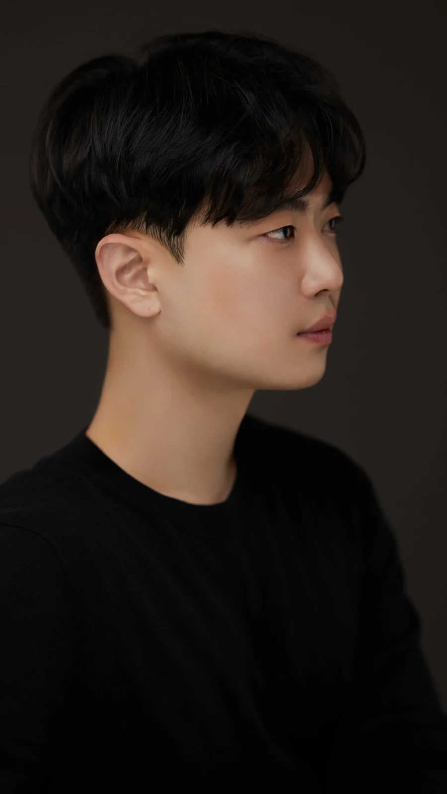 어두운 배경에서 짧은 머리로 옆을 보는 검정 상의 차림 프로필 사진