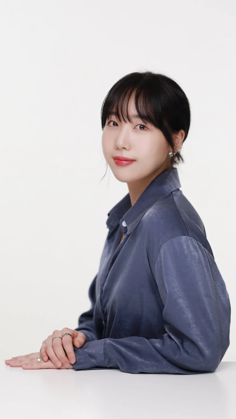 흰 테이블에 팔을 얹고 남색 새틴 셔츠를 입은 프로필 사진