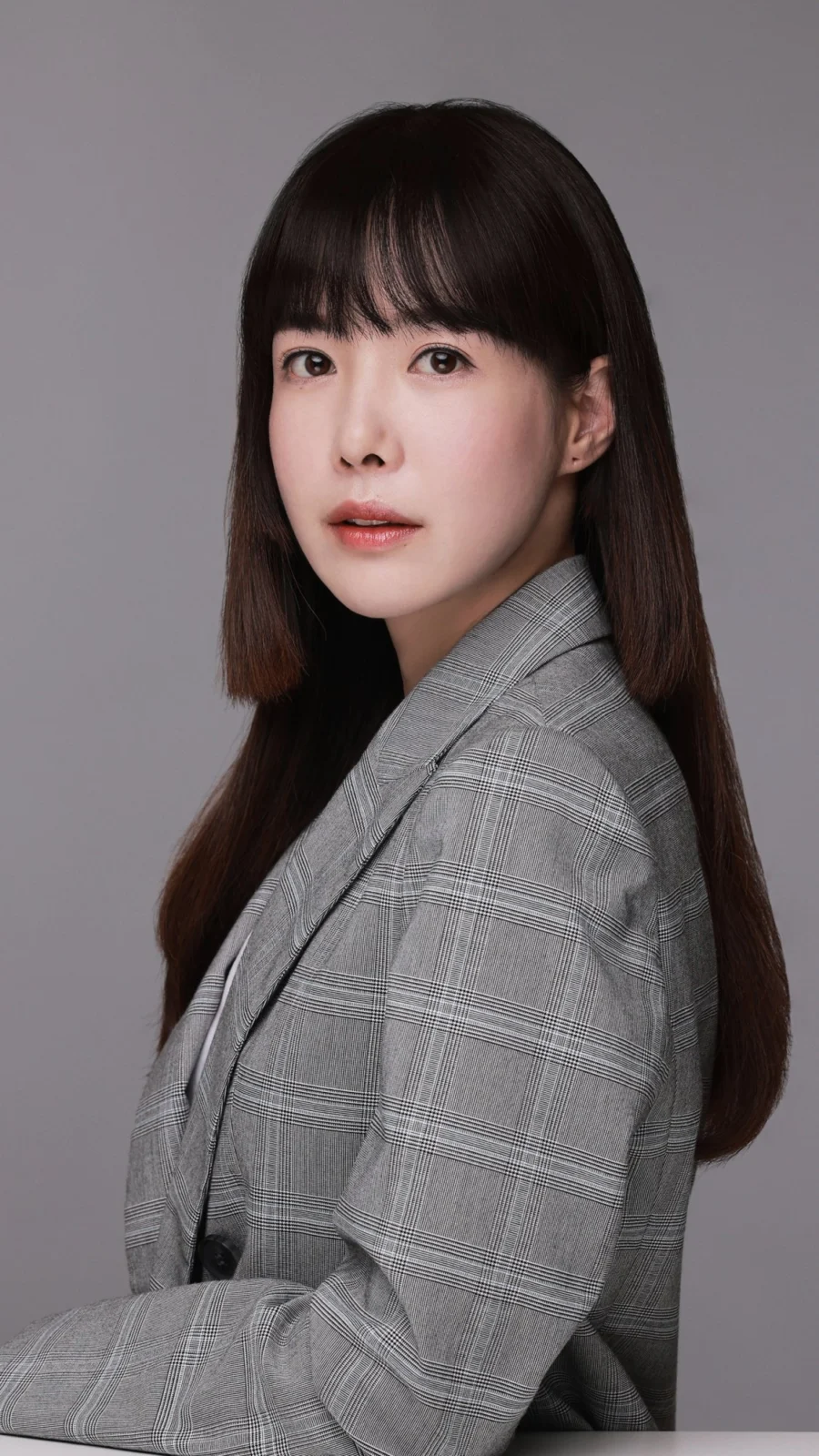 회색 배경에서 앞머리 긴 머리에 체크 재킷을 입은 프로필 사진