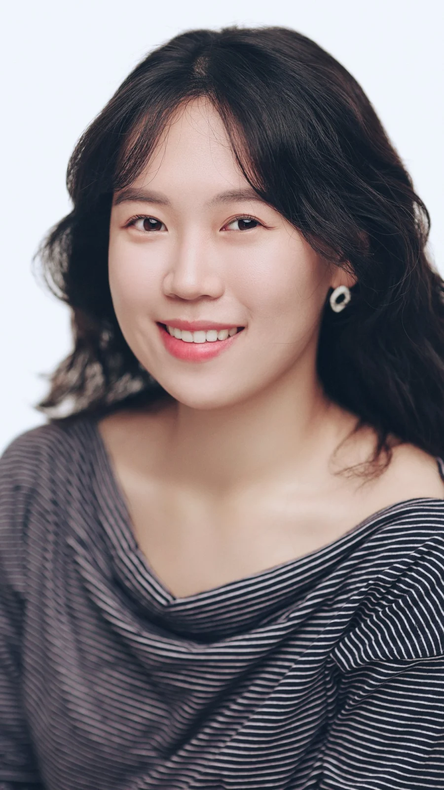 흰 배경에서 웨이브 머리에 줄무늬 상의를 입고 웃는 프로필 사진