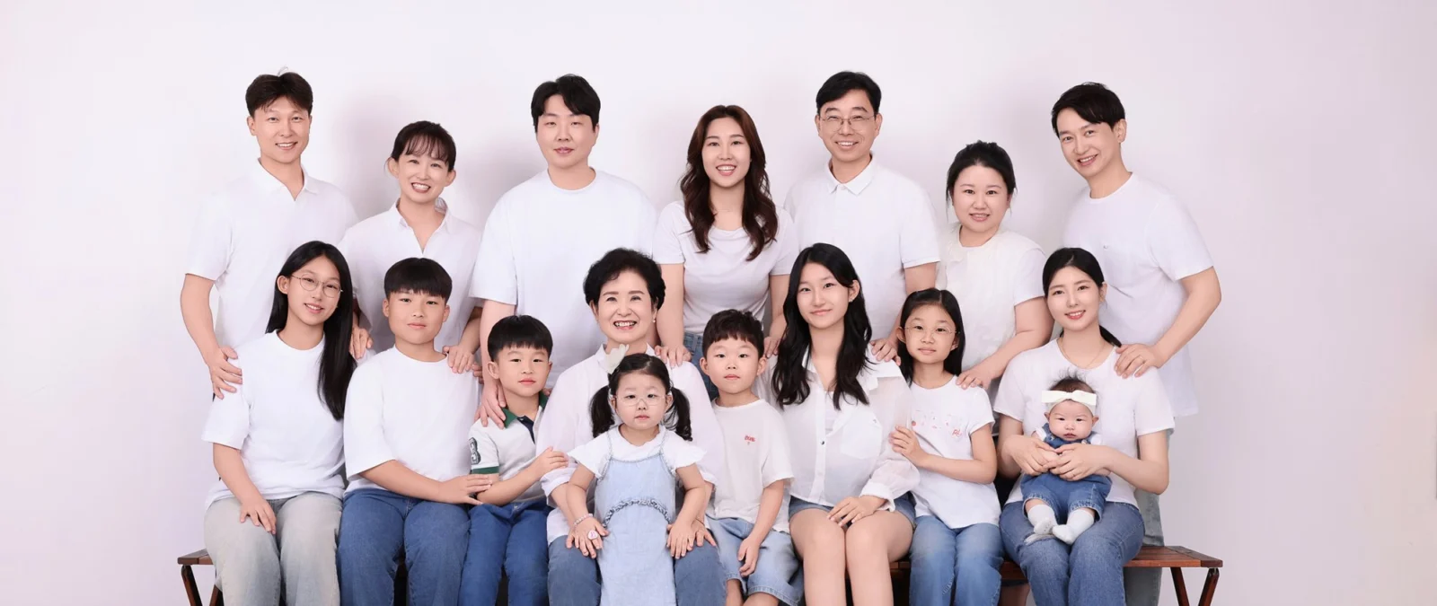 흰 티셔츠와 청바지를 맞춰 입고 두 줄로 모인 열 명이 넘는 대가족 가족사진
