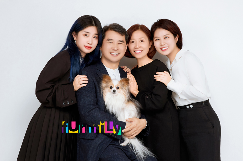 어두운 옷 차림의 네 사람이 모여 선 가운데 긴 털 강아지를 안은 사진, 영문 글자