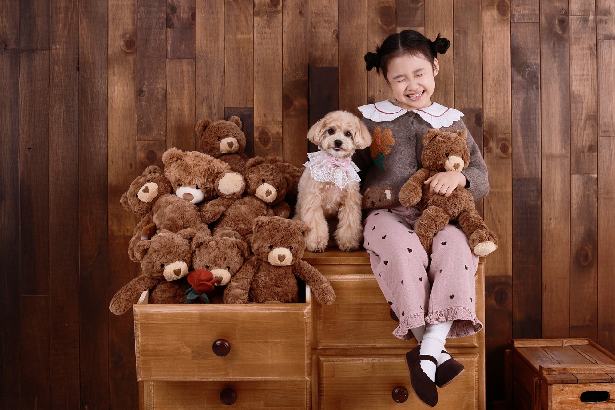 곰 인형 사이 갈색 강아지 옆에서 눈을 감고 웃는 아이의 개족사진