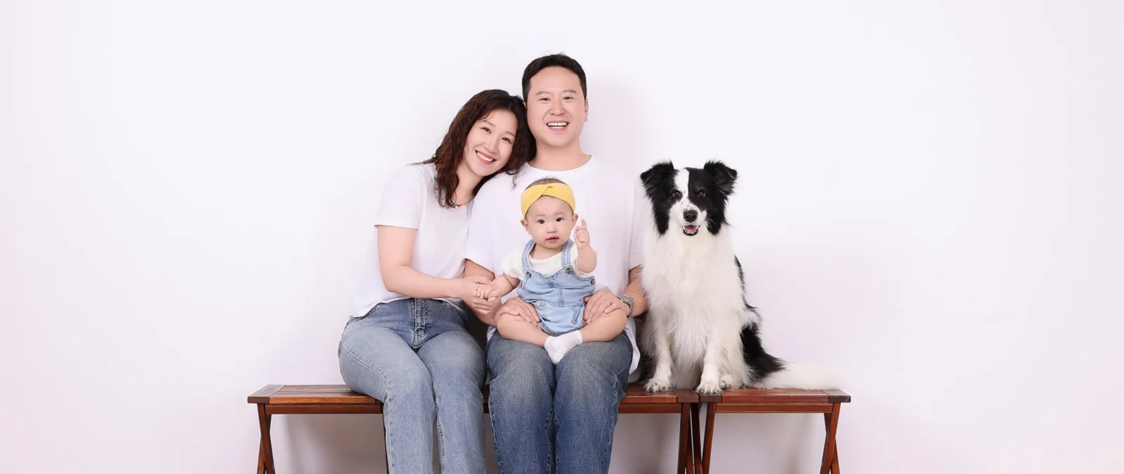 벤치에 앉아 아기를 안은 두 사람 옆에 검은색·흰색 털 개가 앉은 개족사진