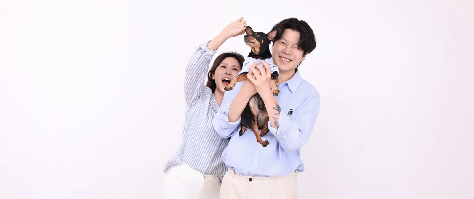 흰 배경에서 갈색 소형견을 머리 위로 들고 웃는 두 사람의 개족사진