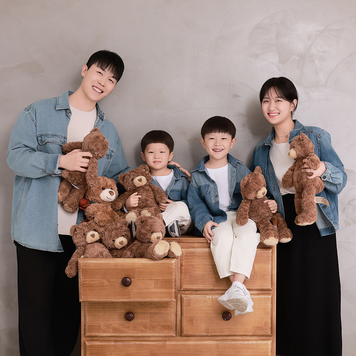 청재킷을 맞춰 입고 곰 인형을 든 네 사람, 둘은 나무 서랍장 위에 앉음