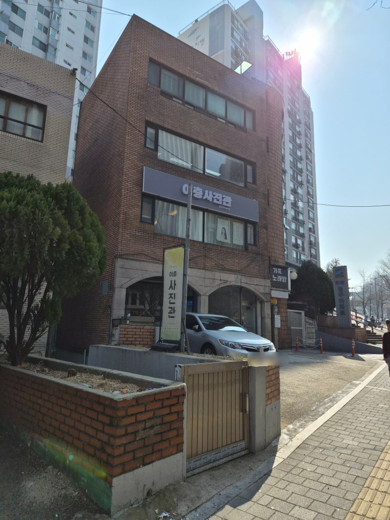 붉은 벽돌 건물 2층에 이층사진관 간판과 세로 입간판이 보이는 거리 모습