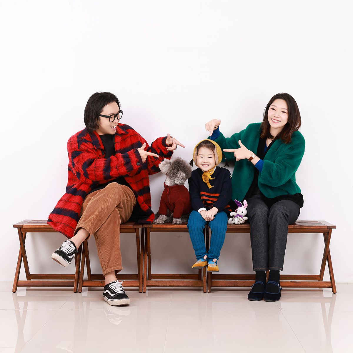 빨강·초록 외투 차림의 두 사람이 벤치 가운데 한 명과 회색 강아지를 가리키는 사진