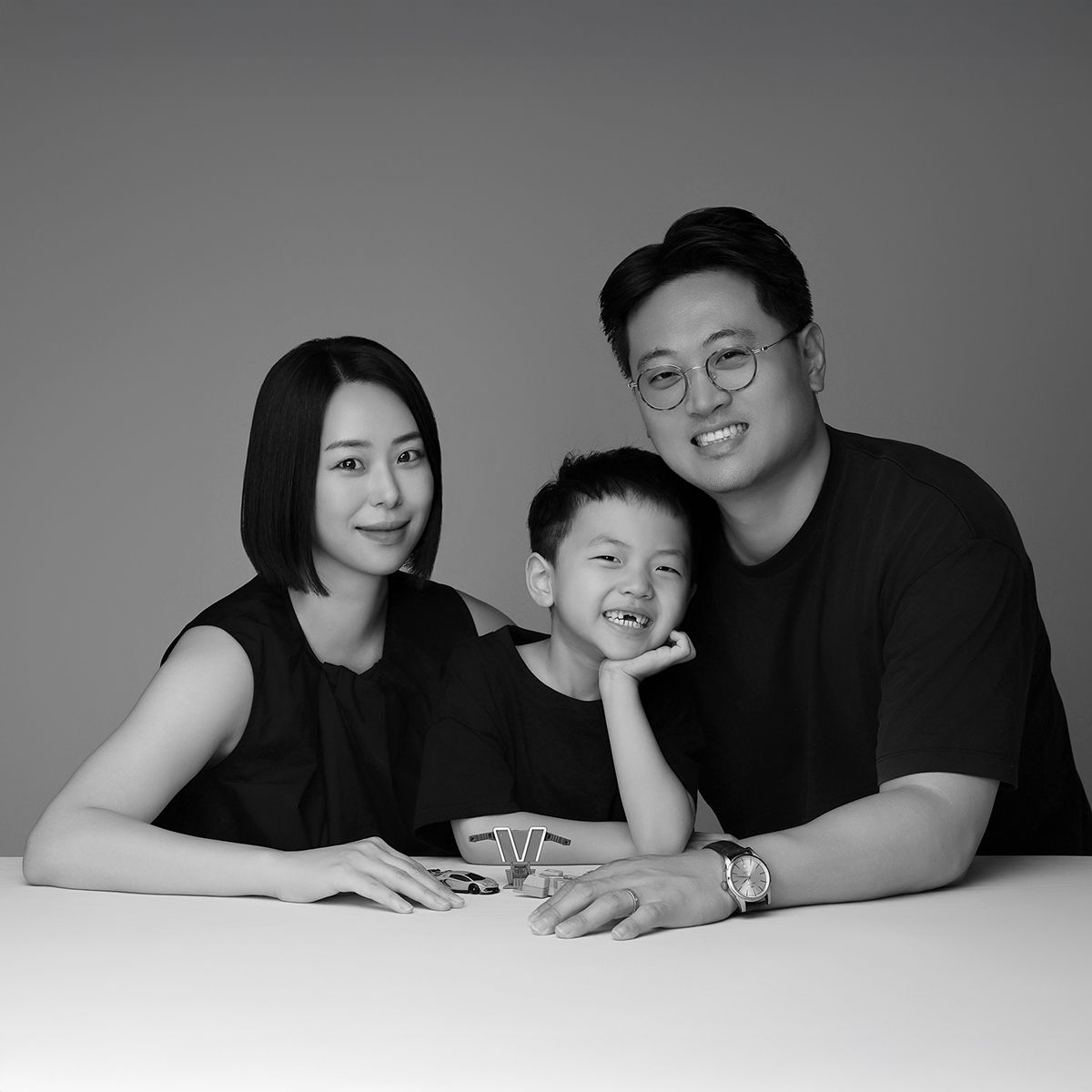 검은 옷을 맞춰 입고 흰 테이블에 팔을 얹고 웃는 세 사람의 흑백 사진