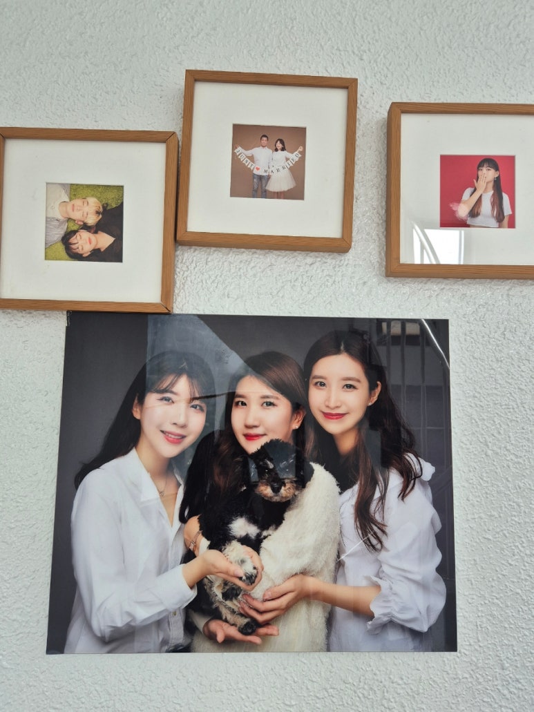 흰 벽에 걸린 작은 사진 액자 세 개와 강아지를 안은 세 사람의 큰 사진