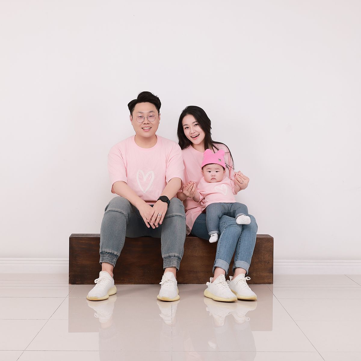 분홍 티셔츠를 맞춰 입고 나무 단 위에 나란히 앉은 세 사람
