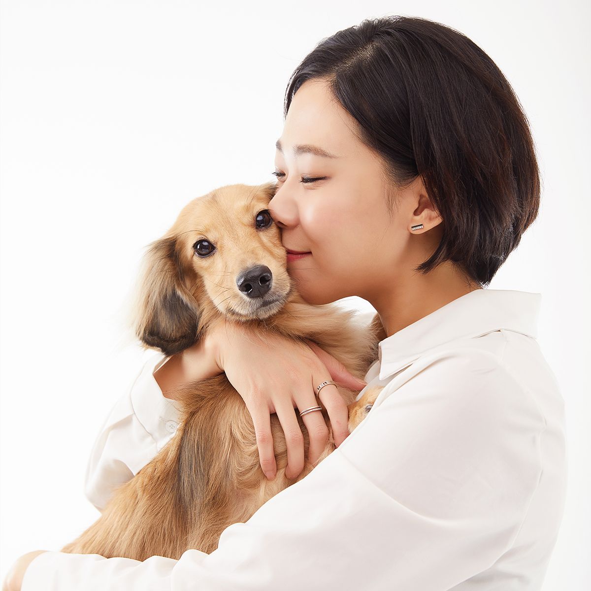 흰 셔츠를 입은 인물이 눈을 감고 긴 털의 갈색 강아지를 꼭 안은 사진