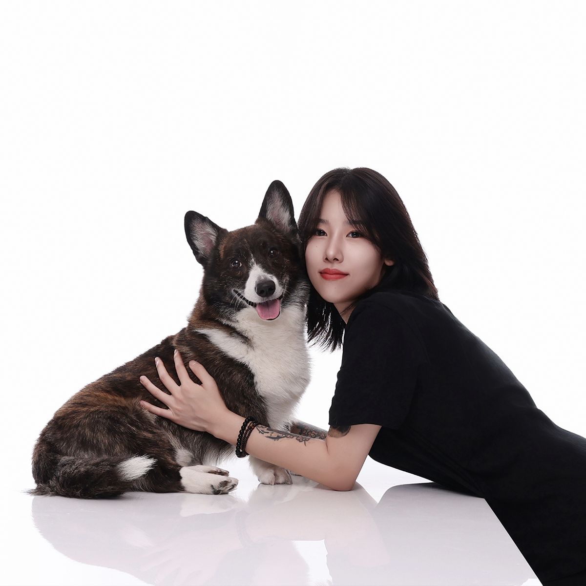 검은 티셔츠 차림의 인물이 흰 바닥에 엎드려 얼룩무늬 강아지를 껴안은 사진