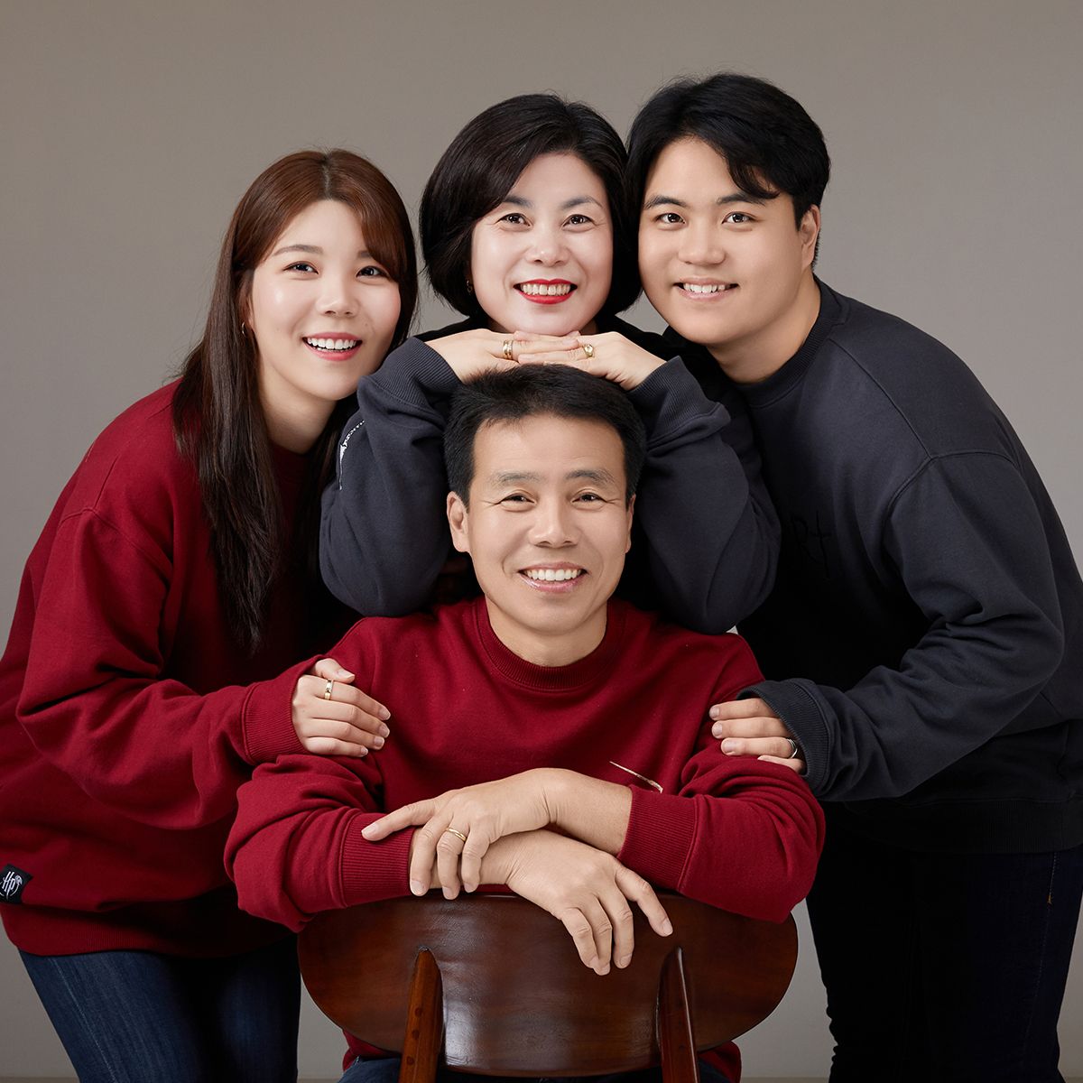 회색 배경 앞 빨강·남색 맨투맨 차림으로 의자 주위에 모인 네 사람