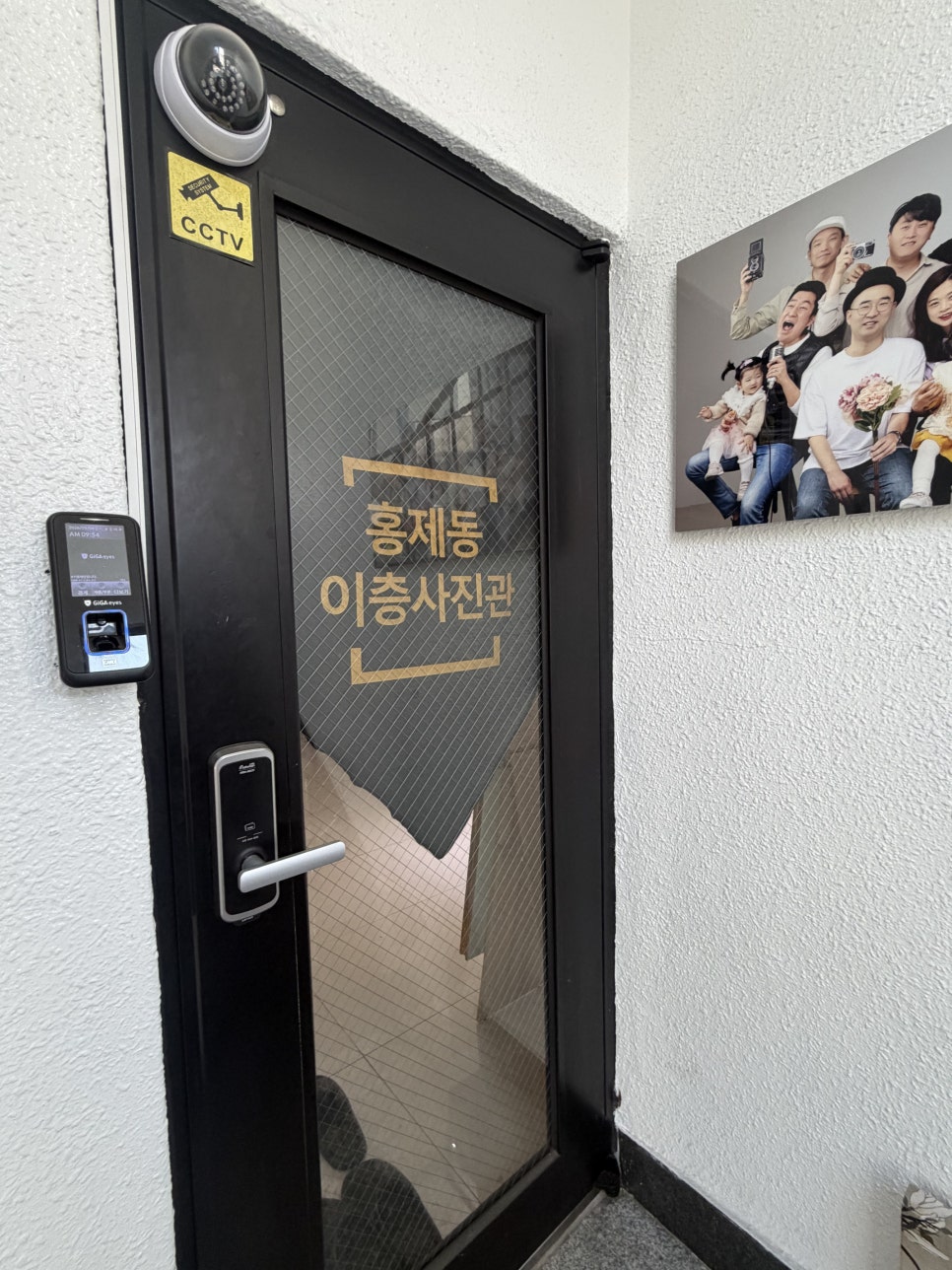 이층사진관 글자가 붙은 검은 유리문과 옆 벽에 걸린 단체 사진 액자