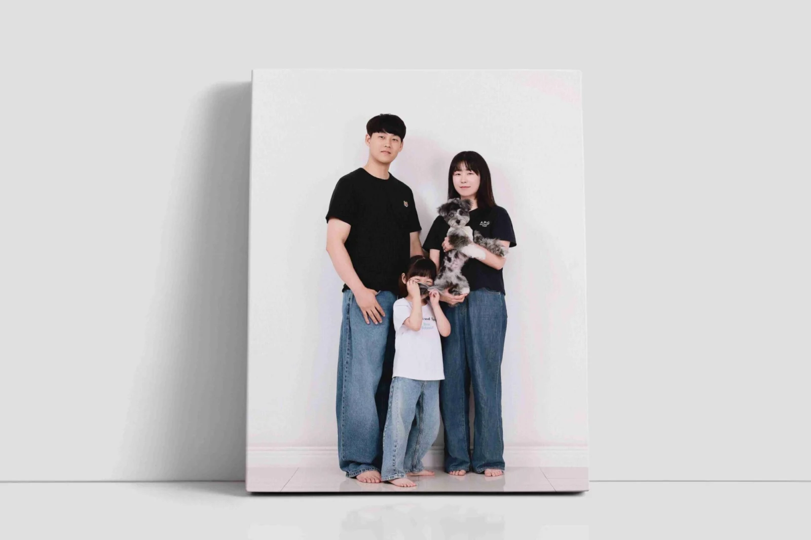 청바지 차림의 세 사람과 회색 얼룩 강아지 사진을 캔버스 액자로 보여 주는 연출