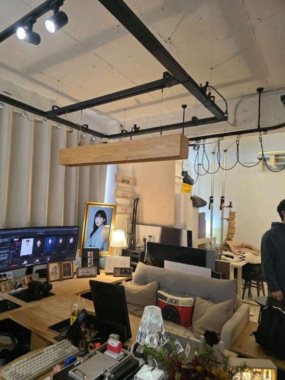 모니터 책상과 소파, 레일 조명과 금색 액자가 보이는 스튜디오 작업 공간