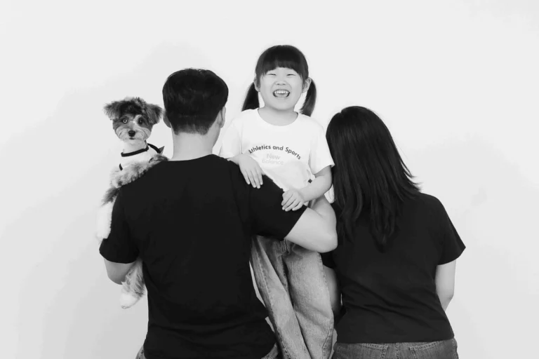 뒤돌아선 두 사람 사이로 한 명이 웃고, 강아지가 어깨 너머 보는 흑백 사진