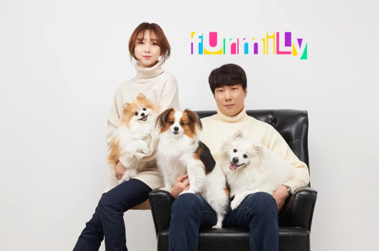 아이보리 니트 차림의 두 사람이 검은 의자에서 털이 긴 강아지 세 마리를 안은 사진