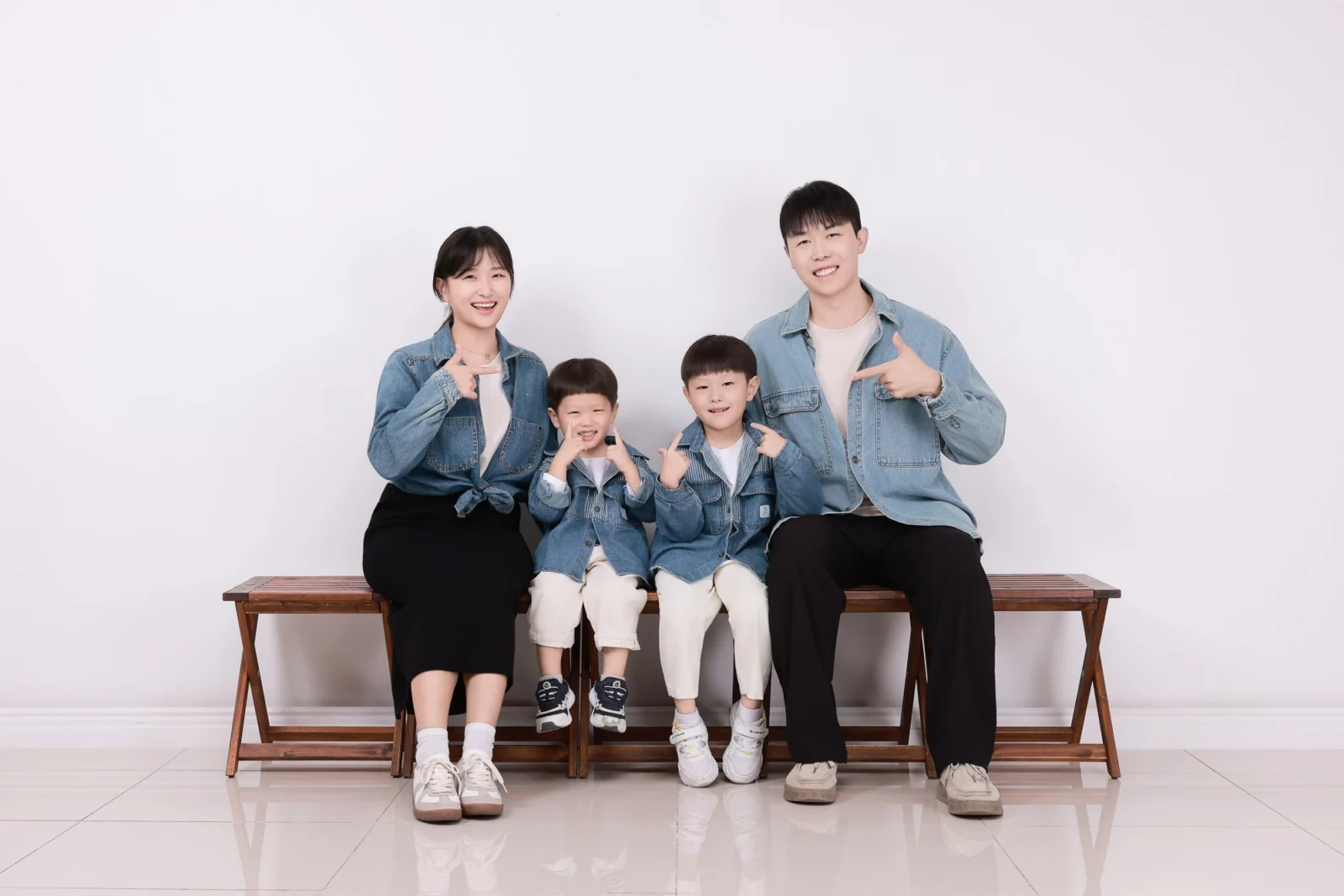 나무 벤치에 앉아 손가락 포즈를 취한 데님 차림 네 명의 가족사진