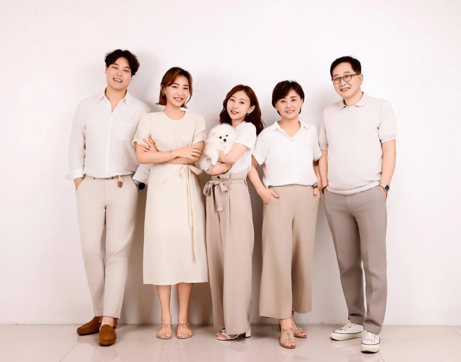 흰색과 베이지 옷을 맞춰 입고 흰 강아지를 안은 다섯 명의 가족사진