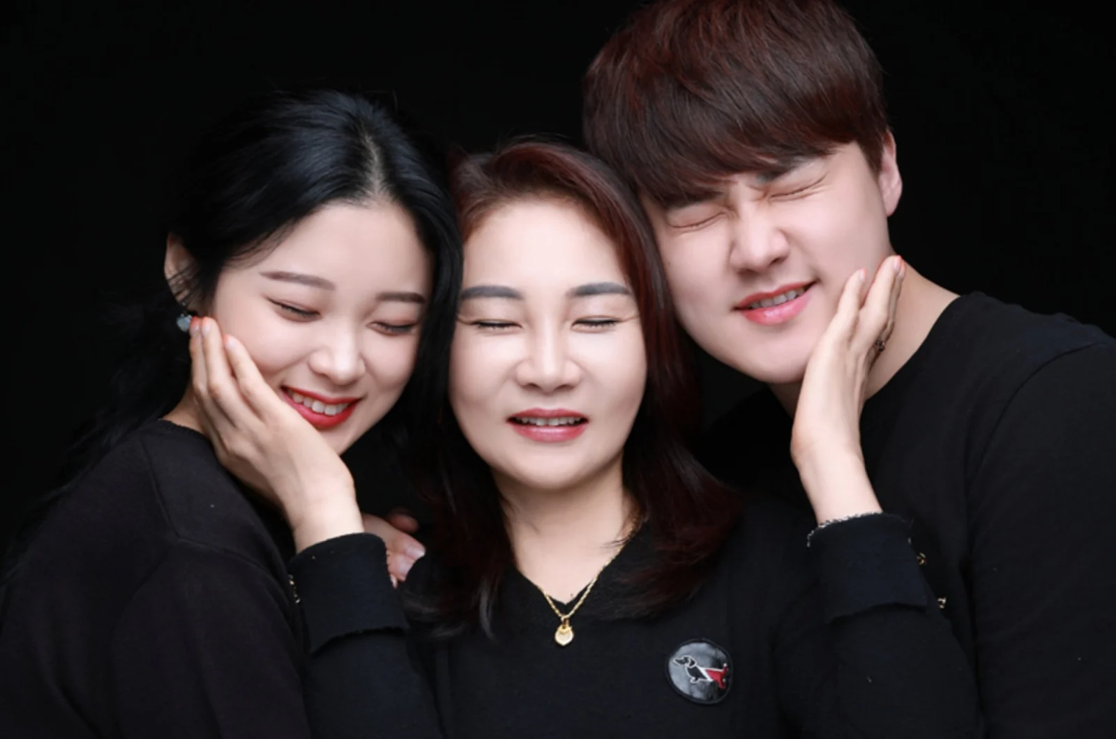 검정 배경에서 볼에 손을 대고 얼굴을 모은 세 사람의 가족사진