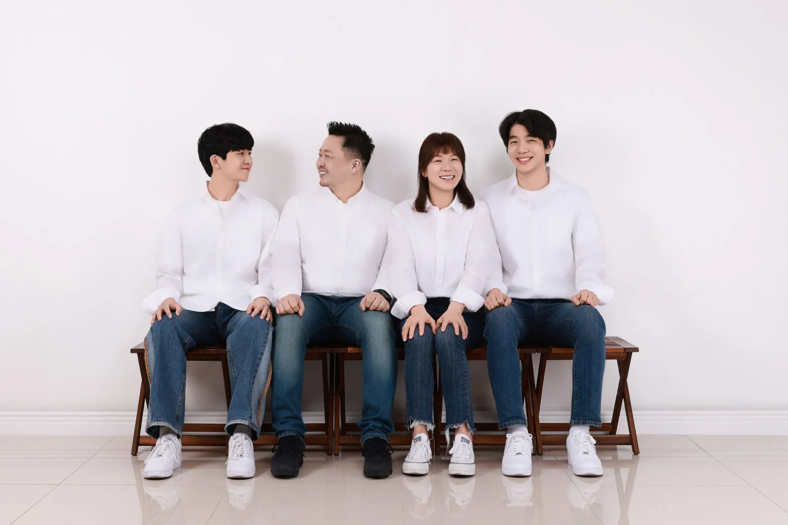 흰 배경 넓은 구도로 흰 셔츠 차림 네 명이 벤치에 앉은 가족사진