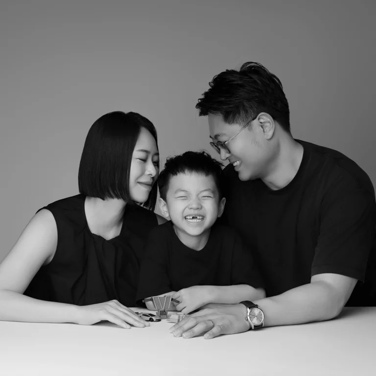 테이블에 팔을 얹고 아이를 사이에 두고 웃는 어른 두 명의 흑백 가족사진