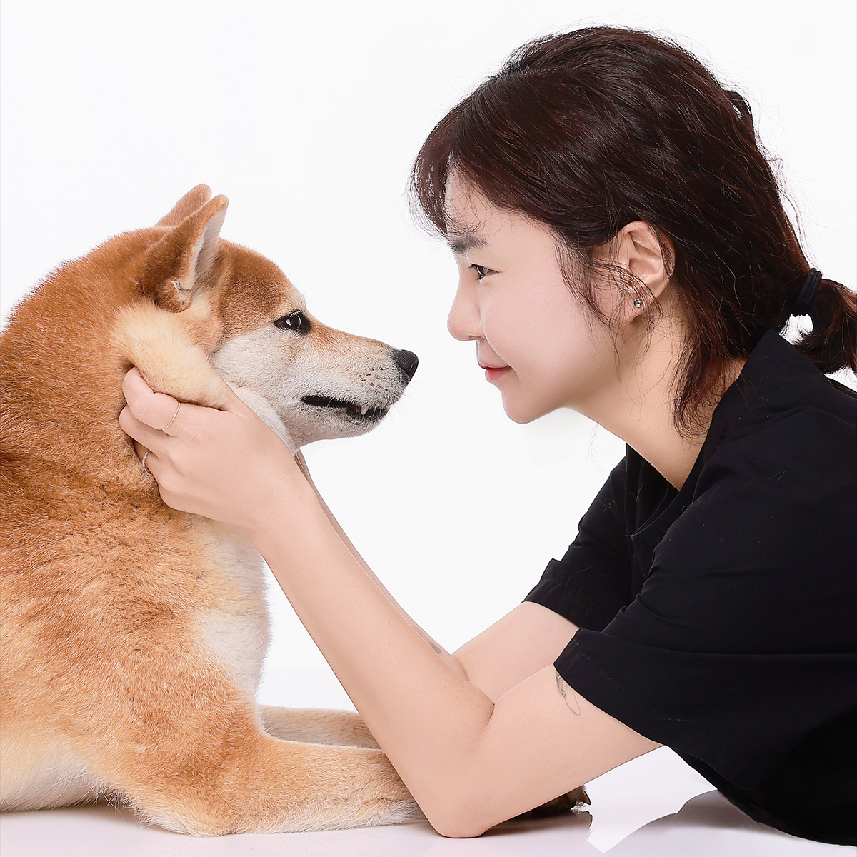 검은 티셔츠 차림의 인물이 황갈색 강아지 얼굴을 감싸고 마주 보는 옆모습