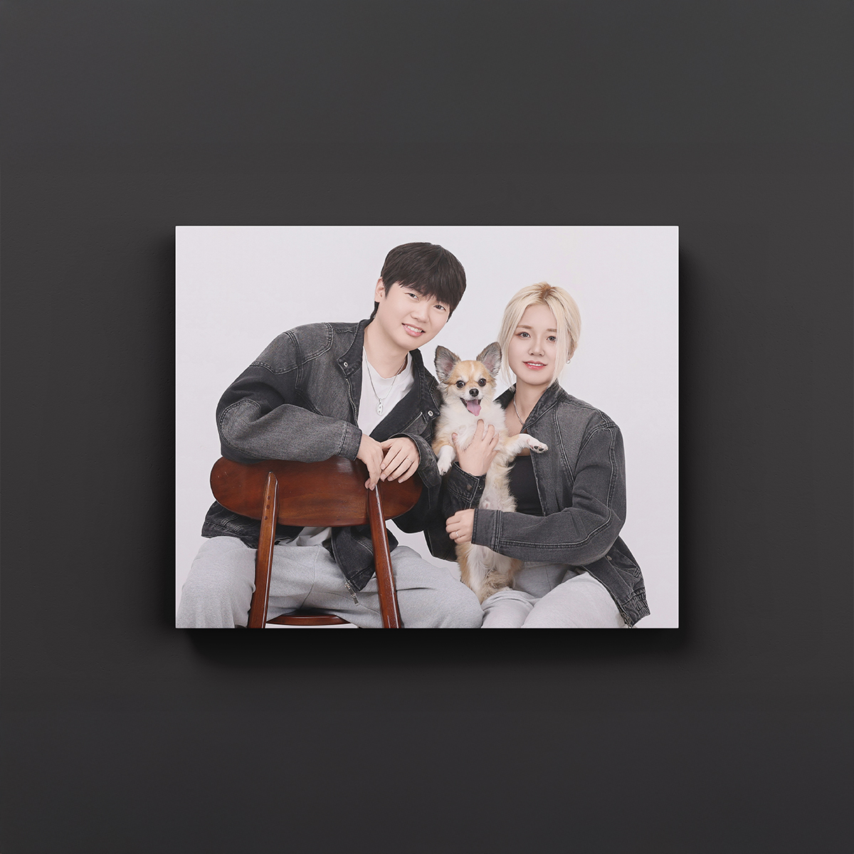 청재킷 차림의 두 사람과 강아지 사진을 캔버스 액자로 보여 주는 연출