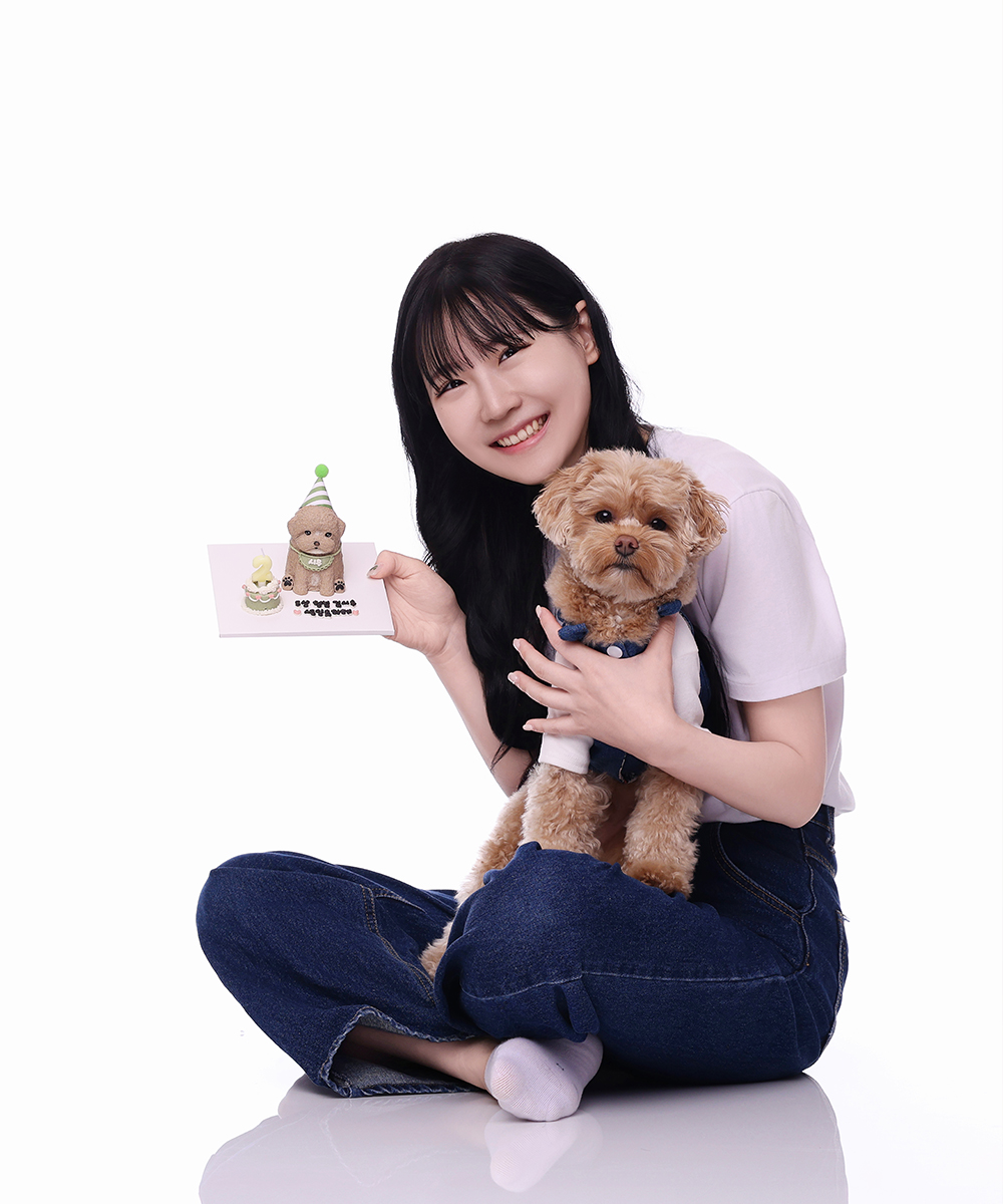 바닥에 앉아 갈색 곱슬 강아지를 안고 강아지 케이크 카드를 든 인물
