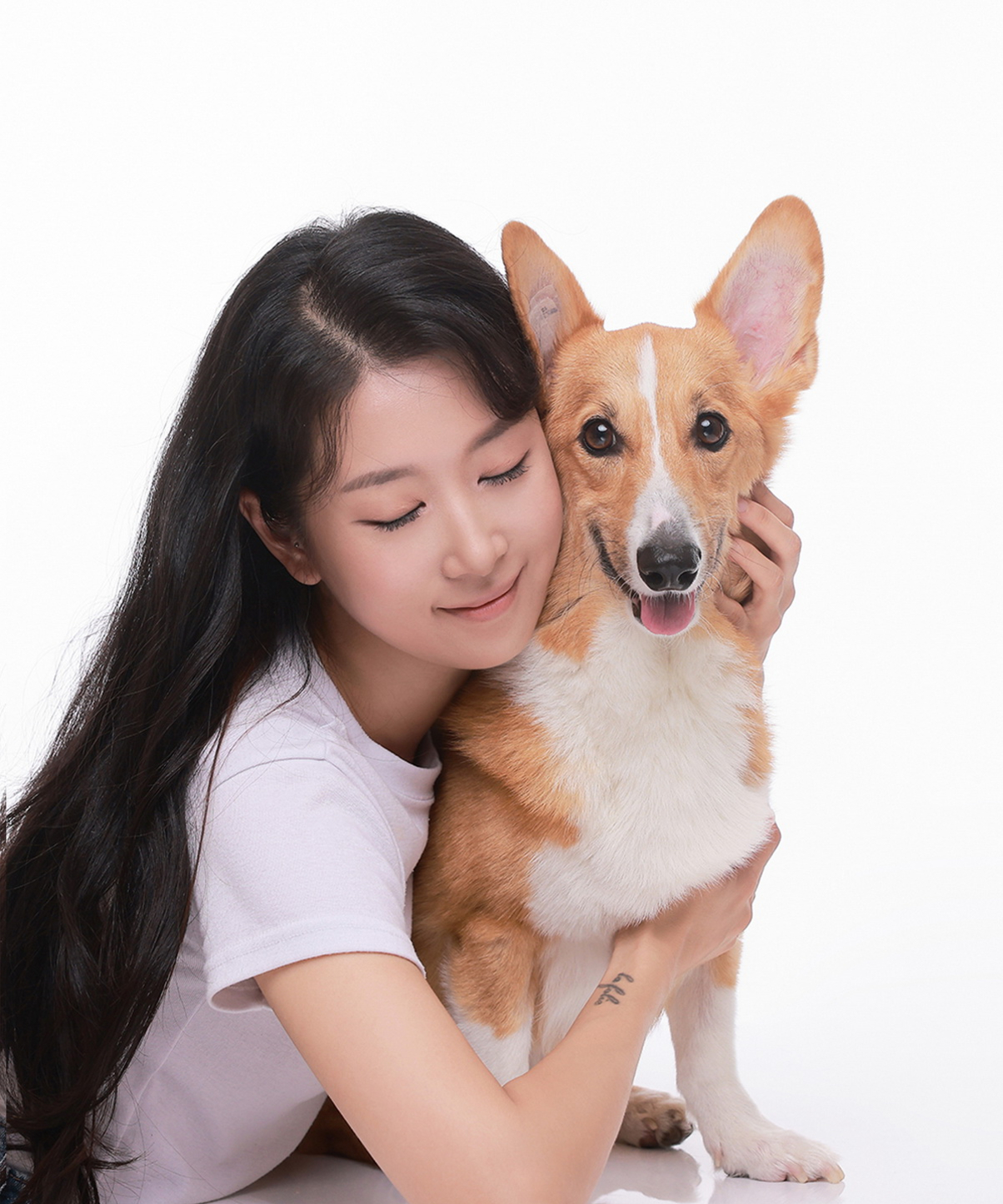흰 티셔츠 차림의 인물이 눈을 감고 귀가 큰 황갈색 강아지를 껴안은 사진