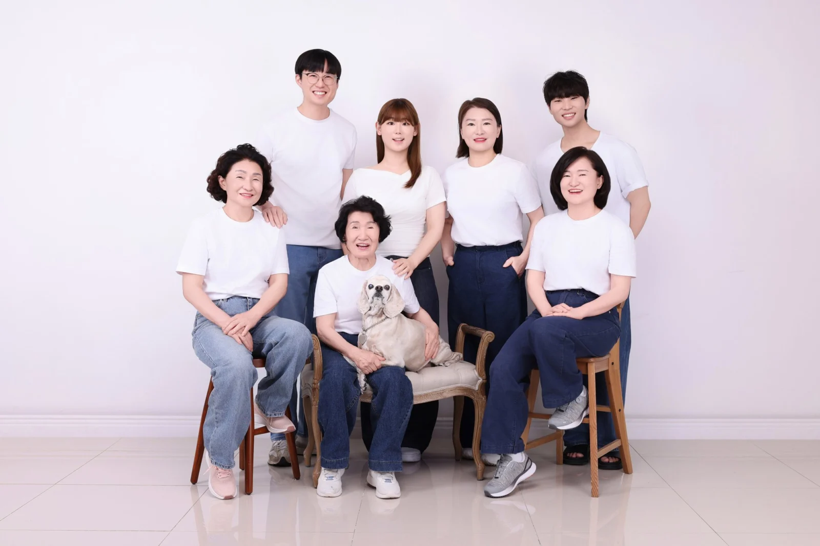 의자에 앉은 세 명 뒤로 네 명이 선 흰 티셔츠 가족과 크림색 강아지의 개족사진
