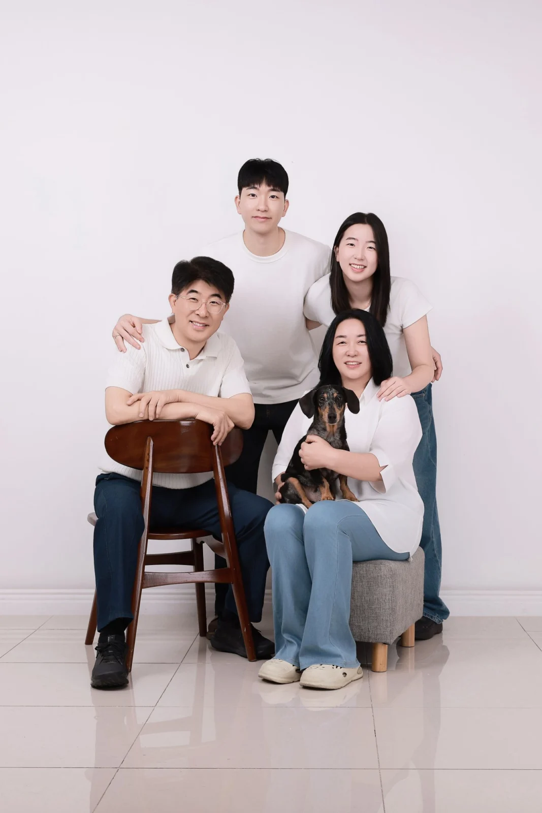 의자와 스툴에 앉고 선 네 명이 검은색·갈색 닥스훈트를 안은 세로 개족사진