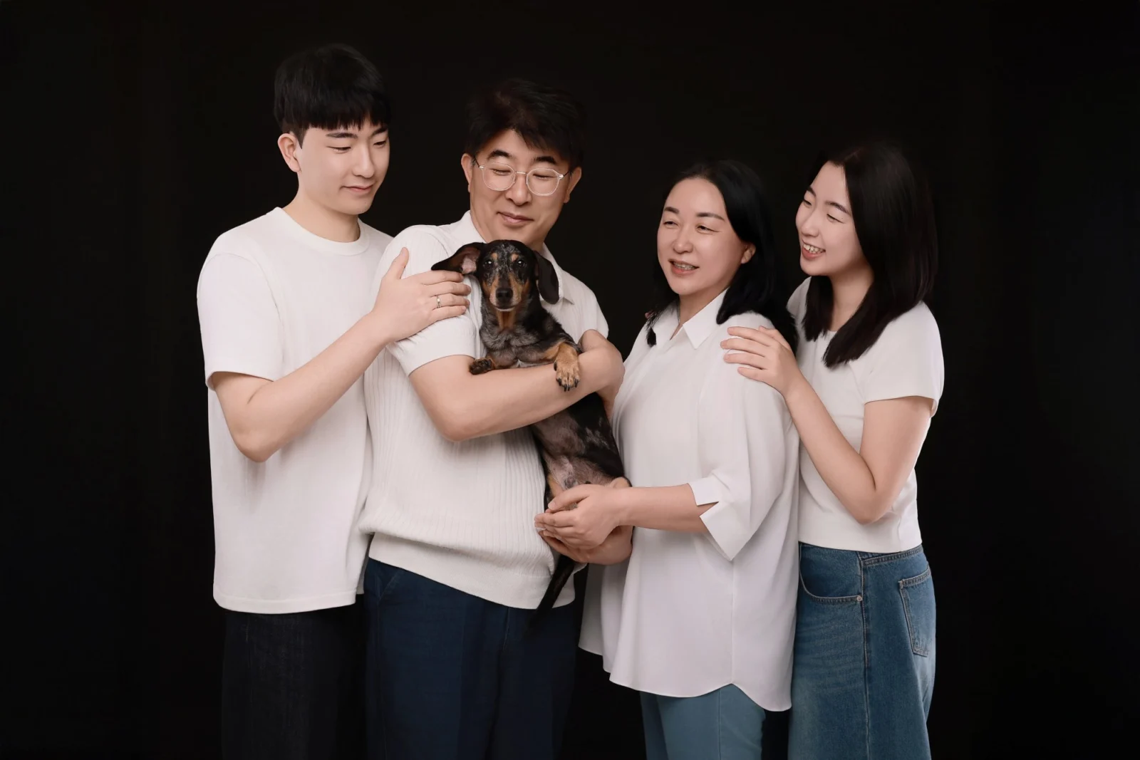 검정 배경에서 흰 상의 차림 네 명이 닥스훈트를 안고 모여 선 개족사진