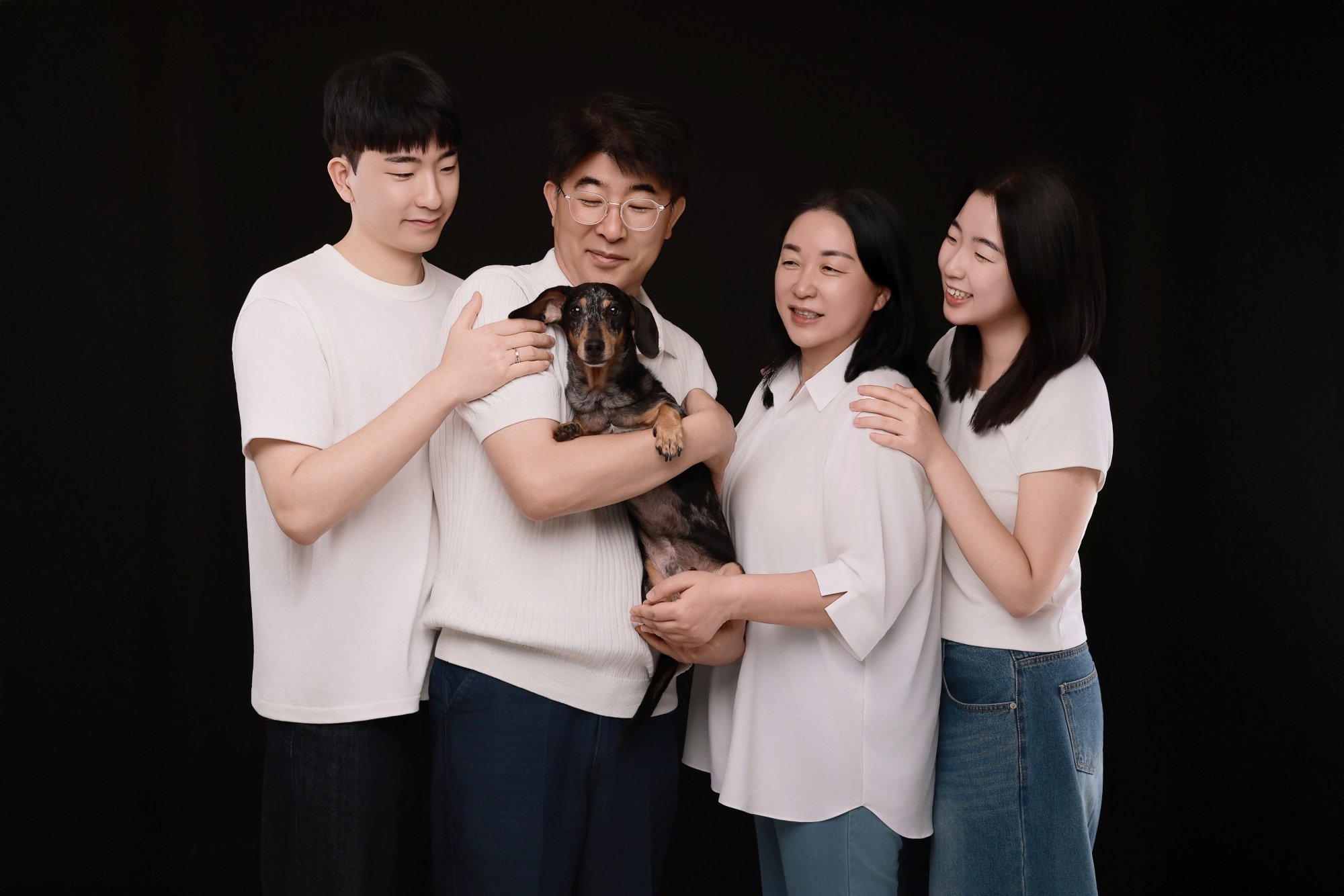 검정 배경에서 흰 상의 차림 네 명이 닥스훈트를 안고 모여 선 개족사진