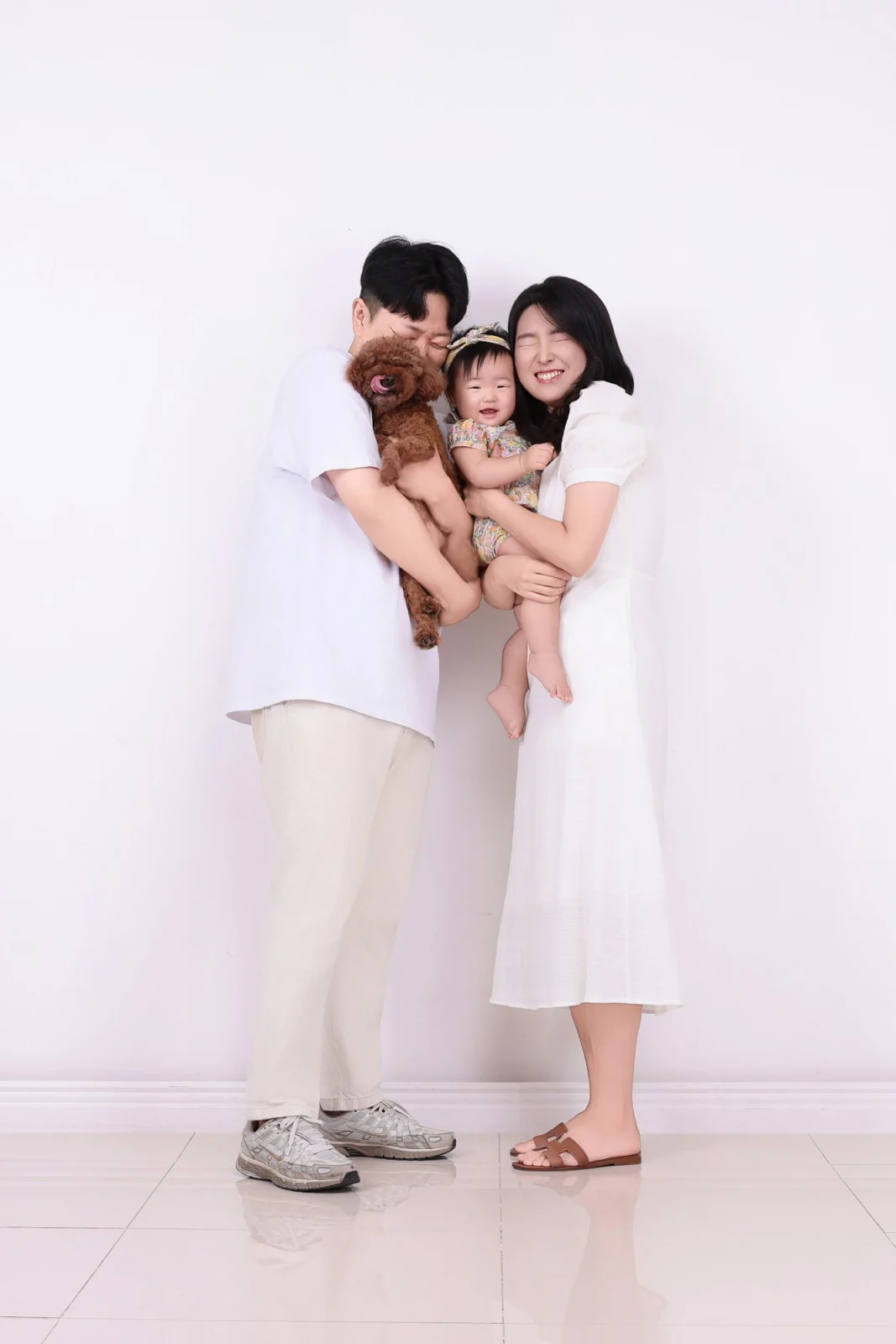 흰 옷 차림 두 사람이 아기와 갈색 곱슬털 강아지를 함께 안고 선 세로 개족사진