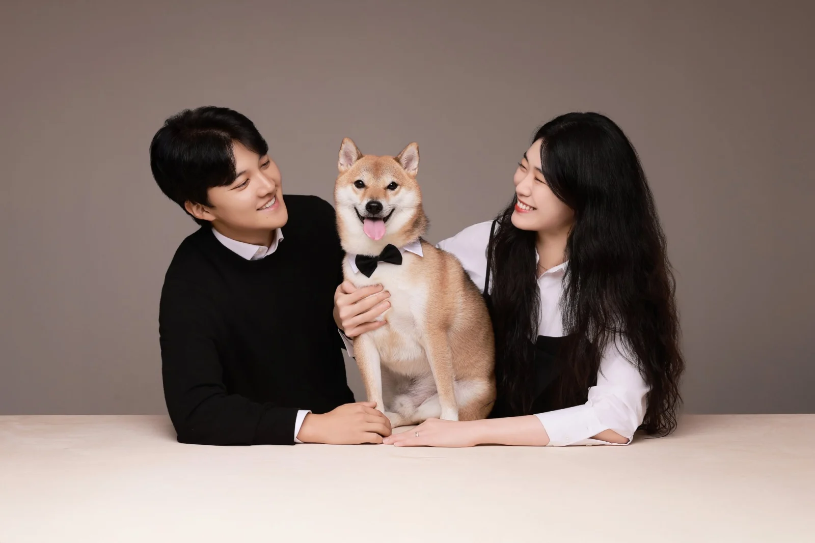 갈색 배경 테이블에서 갈색 개를 가운데 두고 서로 바라보는 두 사람의 개족사진