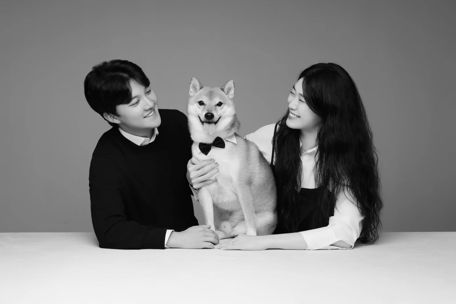 테이블에서 개를 가운데 두고 서로 바라보는 두 사람의 흑백 개족사진