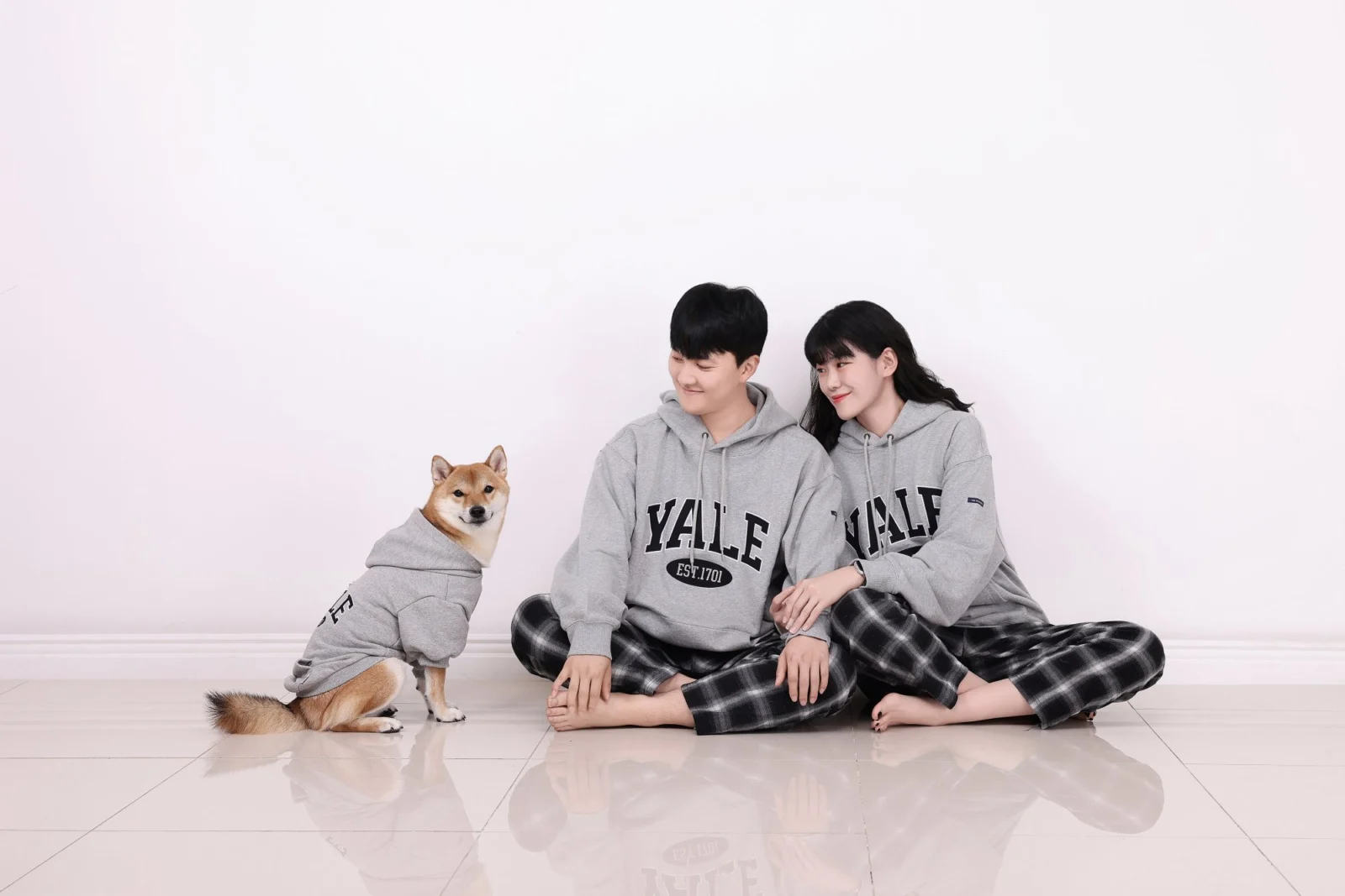 옷 입은 갈색 개와 나란히 바닥에 앉아 서로 기댄 두 사람의 개족사진