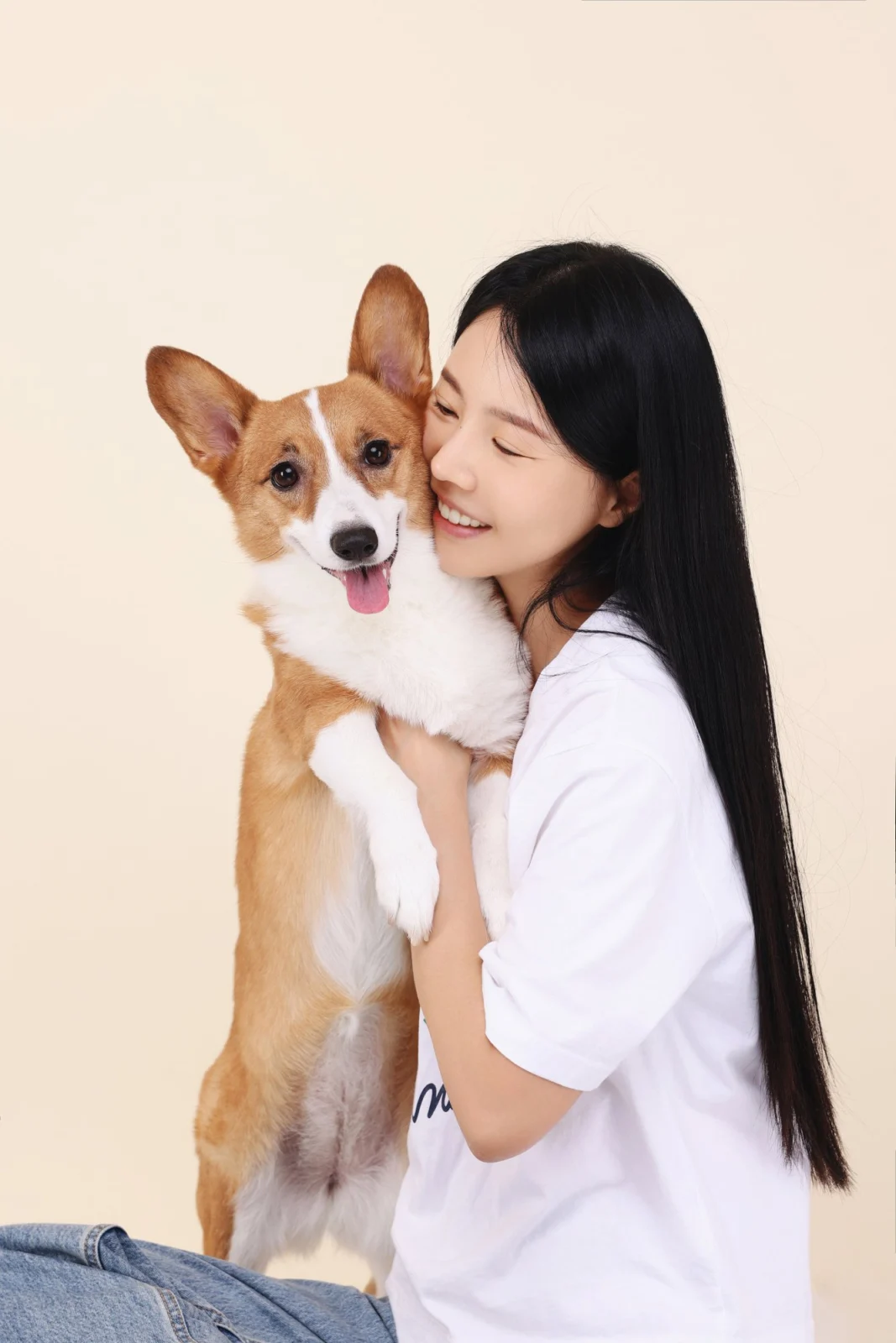 크림색 배경에서 일어선 웰시코기를 끌어안고 웃는 한 사람의 둘이함개 사진