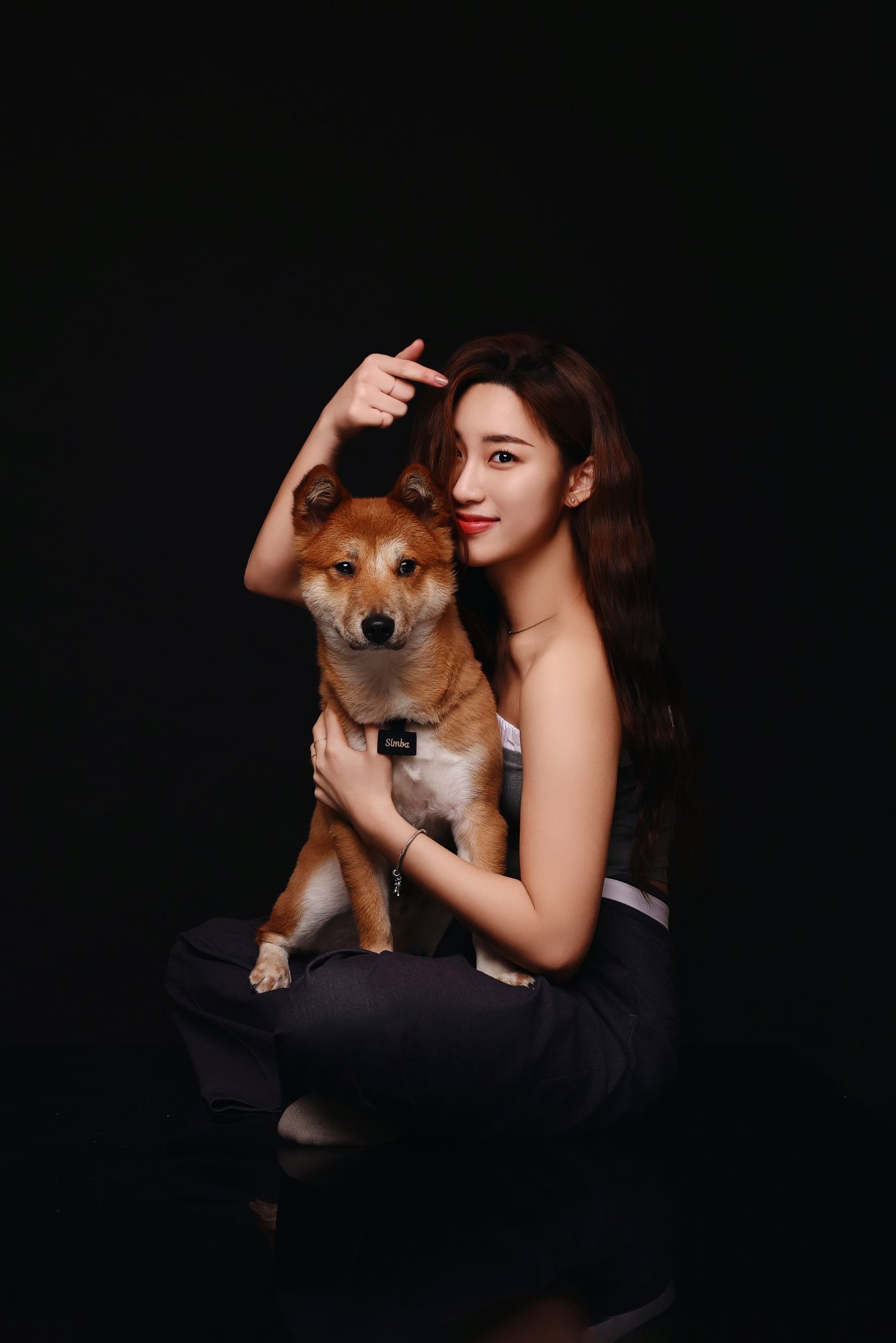검정 배경에서 시바견을 무릎에 안은 여성