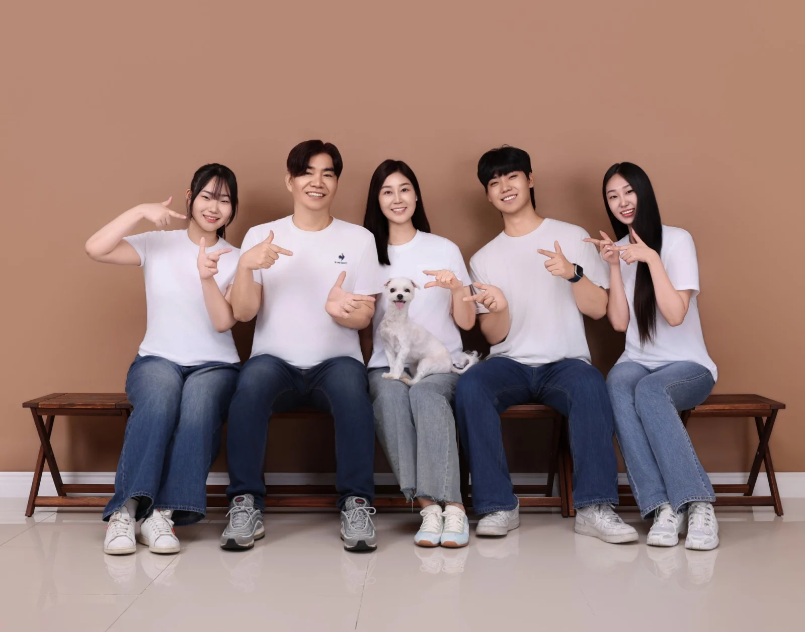 갈색 배경 벤치에서 흰 강아지를 가운데 두고 손 포즈를 한 다섯 명의 개족사진