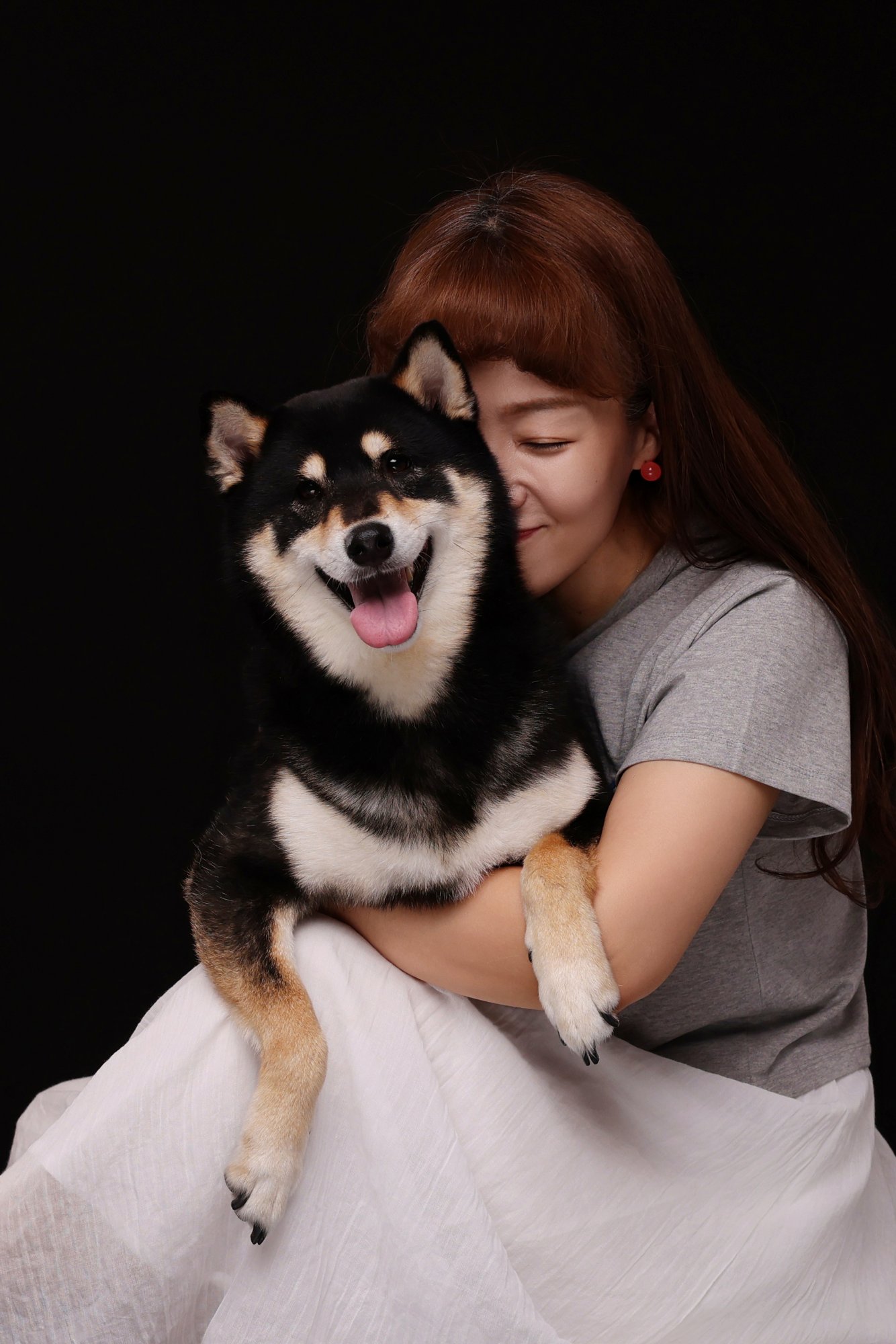 검정 배경에서 블랙탄 시바견을 안고 볼을 댄 여성
