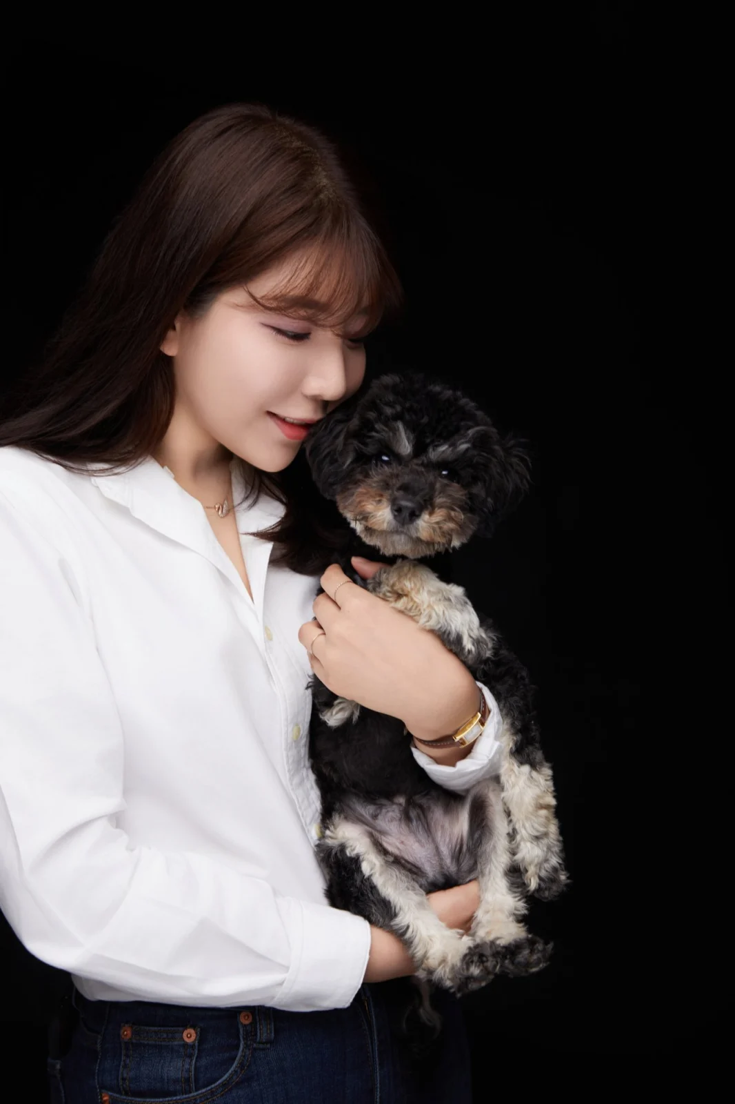 검정 배경에서 검은색·흰색 곱슬털 소형견을 안고 볼을 댄 한 사람의 개족사진
