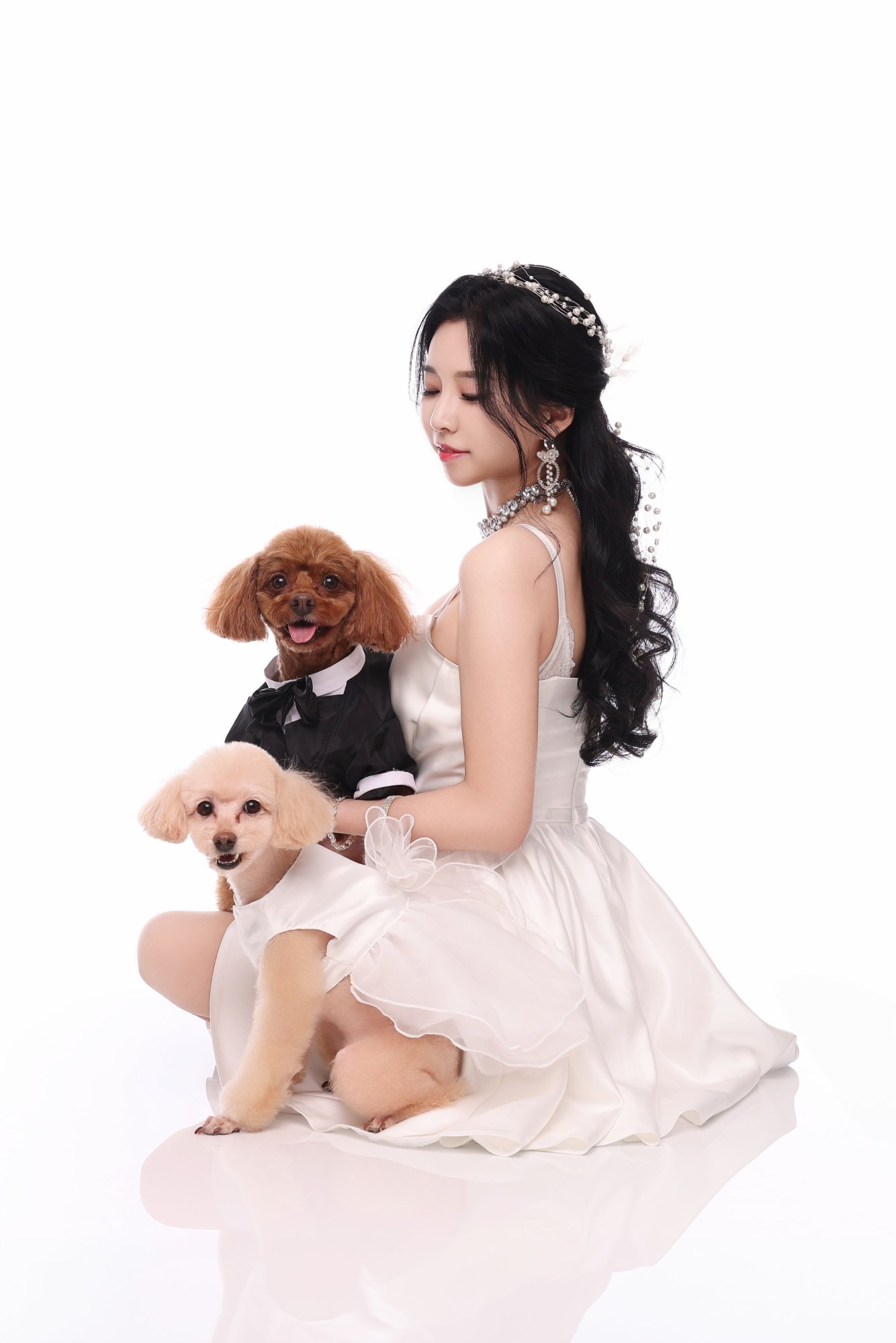 턱시도와 드레스를 입힌 푸들 두 마리를 안은 여성