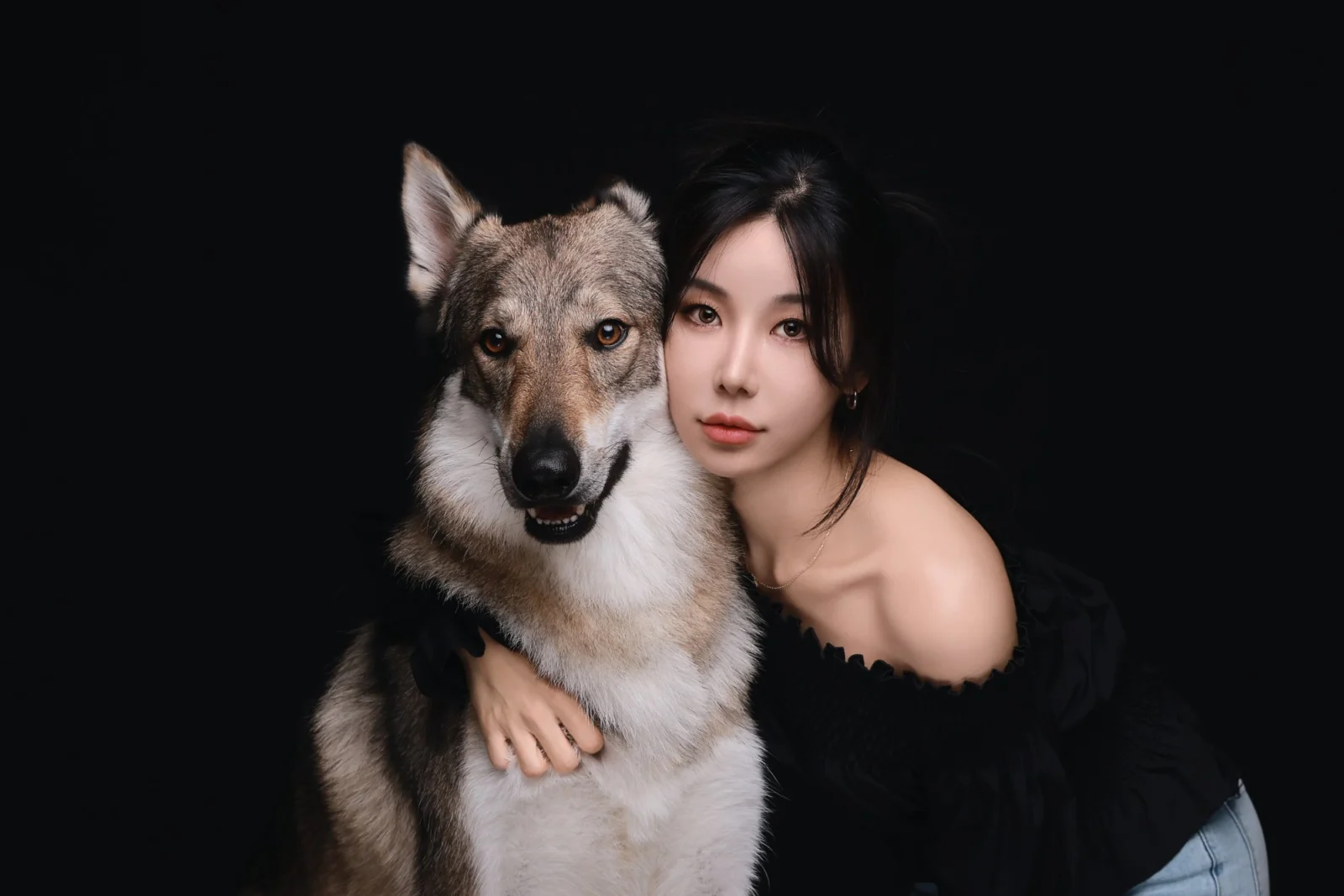 검정 배경에서 회갈색 대형견에게 얼굴을 기대고 안은 한 사람의 둘이함개 사진