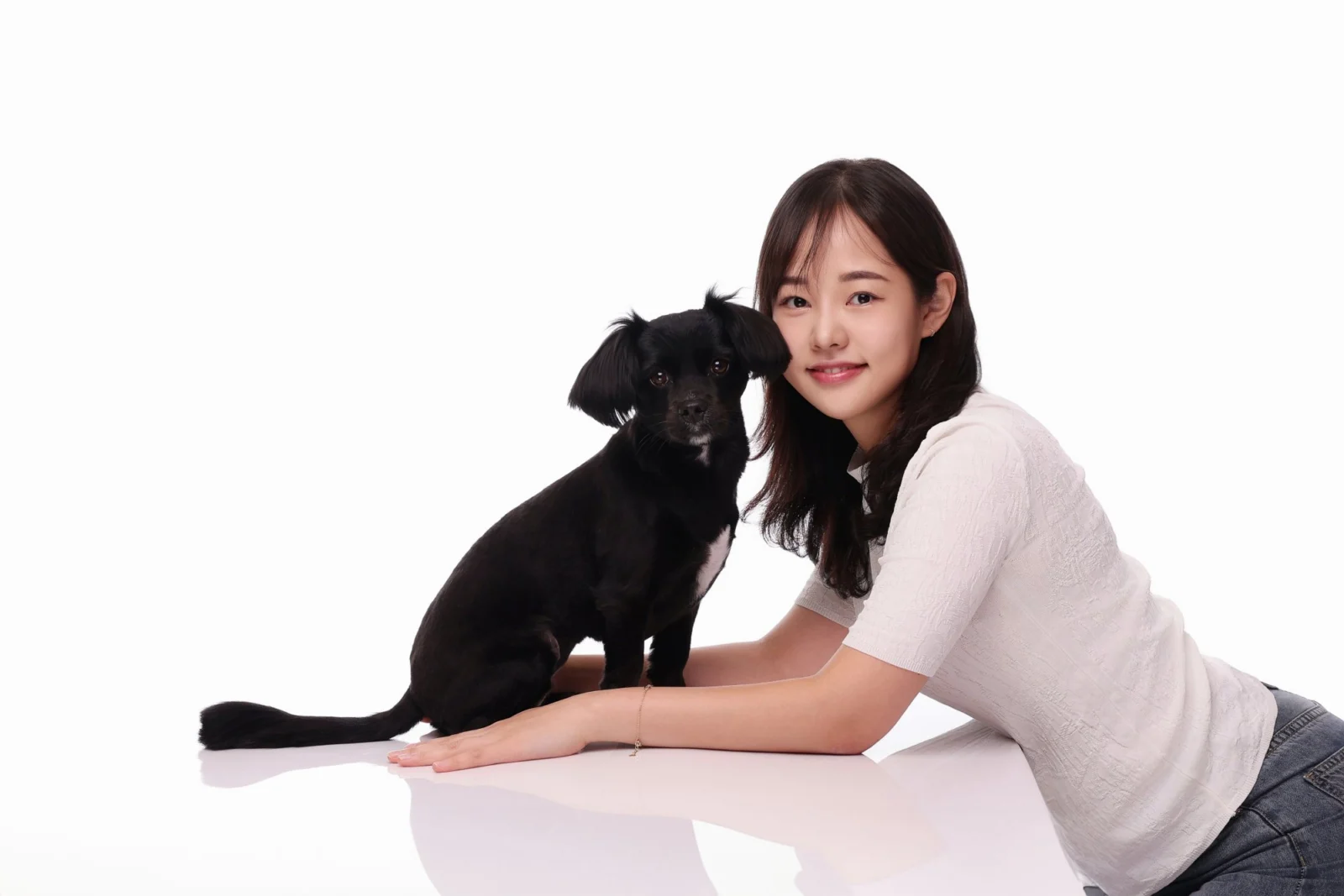 흰 바닥에 엎드린 한 사람 옆에 검은 소형견이 앉은 가로 둘이함개 사진